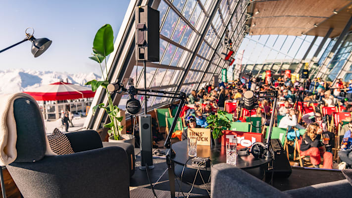 Eine Bühne mit Stühlen, Mikrophonen und ein Publikum in Skikleidung.