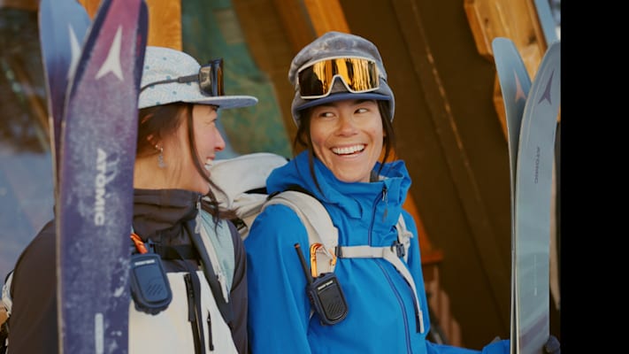 Zwei Freundinnen sehen sich an und lachen sich an in SKikleidung.