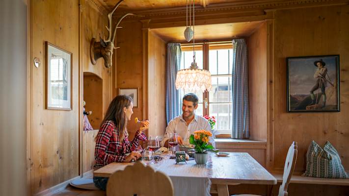 Paar sitzt in einer urigen Hütte und genießt ein Glas Wein und gutes Essen in Schenna