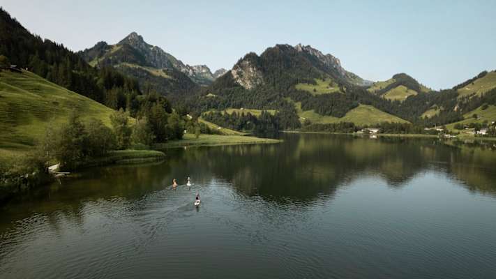 Drei Stand Up Paddler gleiten über das dunkle Wasser des Schwarzsees.