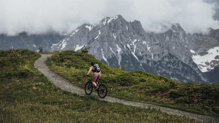 Eine Frau fährt mit dem MTB auf einem aussichtsreichen Höhenweg.