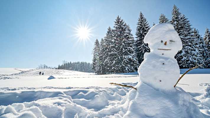 Ein Schneemann steht vor einer sonnigen Winterlandschaft.