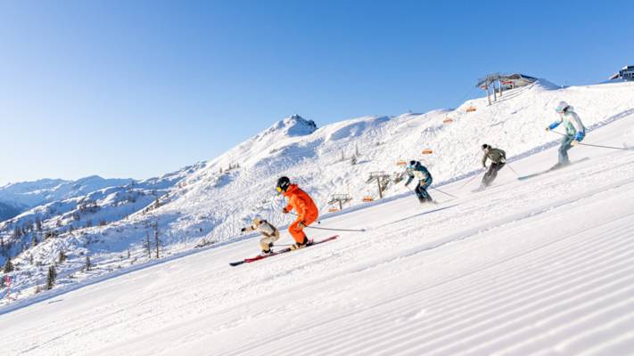 Fünf Skifahrer fahren eine perfekte präparierte Piste in Flachau hinunter.