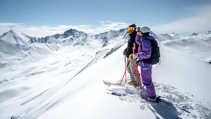 Ein Skifahrer und eine Skifahrerin stehen auf einem Berg und genießen das schneereiche Panorama im Paznaun.