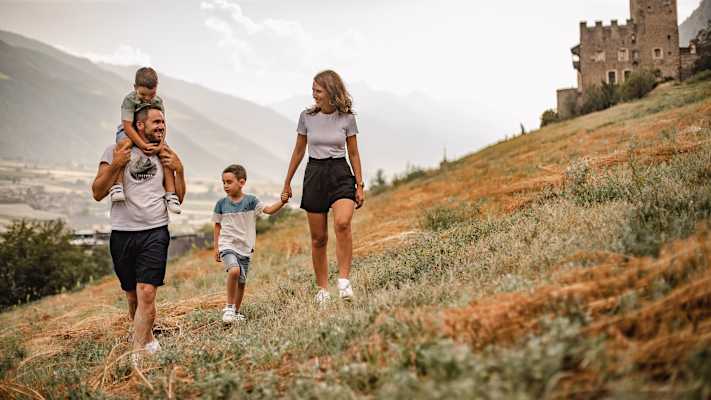 Eine vierköpfige Familie geht über eine Wiese in Naturns.