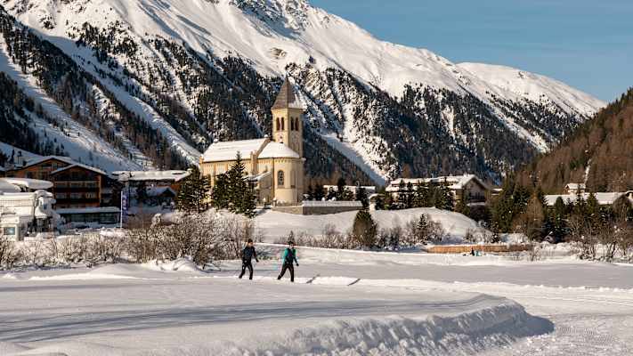 Eine Langläuferin und ein Langläufer gleiten eine Loipe im Ortlergebiet entlang.