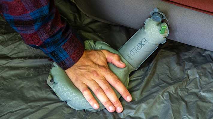 Eine Hand drückt auf die Mini Pump von Exped, um eine Schlafmatte aufzublasen.