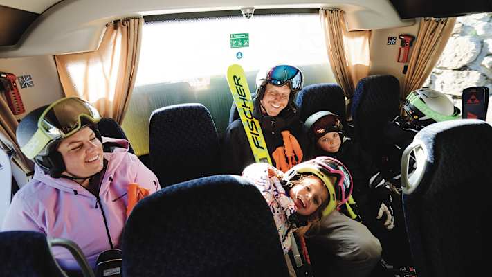 Eine fünfköpfige Familie sitzt in einem Bus-Shuttle in der letzten Reihe und fährt in Richtung Skigebiet Kappl.