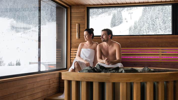 Eine Frau und ein Mann sitzen in der Therme in Gastein und blicken auf die Schneelandschaft.