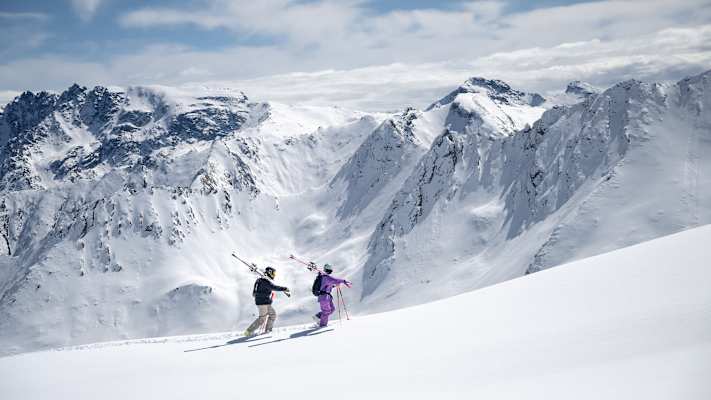 Zwei Freerider gehen einen unberührten Schneehang entlang.
