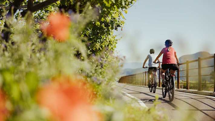 Eine Radfahrerin und ein Radfahrer fahren eine gut ausgebaute Radstrecke in Naturns entlang.