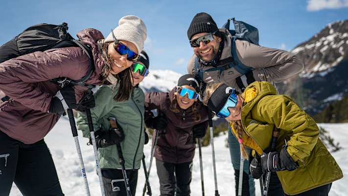Eine fünfköpfige Familie ist auf Skitour und lächelt für ein Gruppenfoto in die Kamera.
