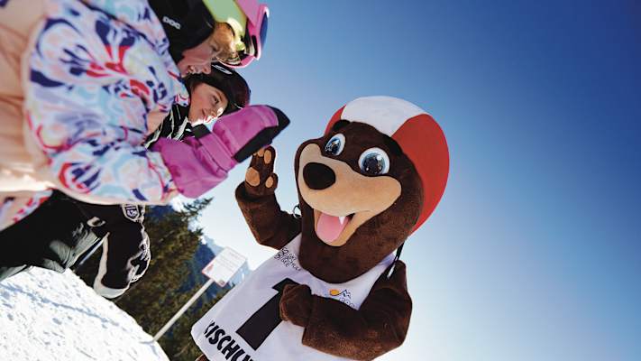 Seebi das Maskotchen der Skischule See gibt zwei Kindern ein High-Five.
