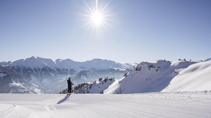 Ein Skifahrer steht im Nationalpark Hohe Tauern auf der Skipiste und genießt das Bergpanorama im Sonnenschein.