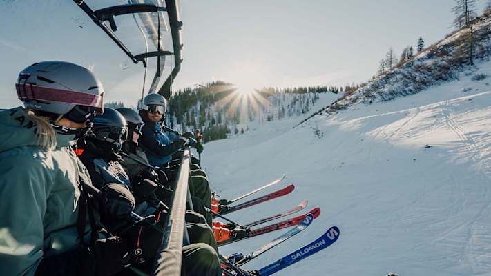 Eine vierköpfige Familie sitzt auf einem Sessellift und genießt den Ausbilck.