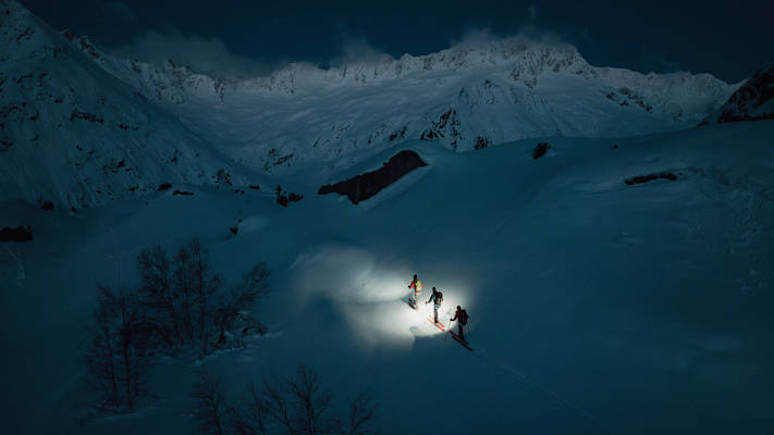 Drei Skitourengeher gehen in der Dunkelheit eine Tour in den Schweizer Alpen.