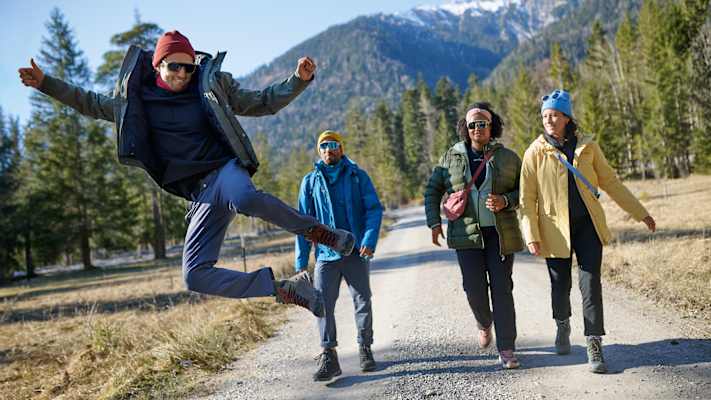 Gruppe von Wanderern in funktionaler Outdoorbekleidung von Maier Sports auf einem Waldweg, umgeben von Bergen und Natur.