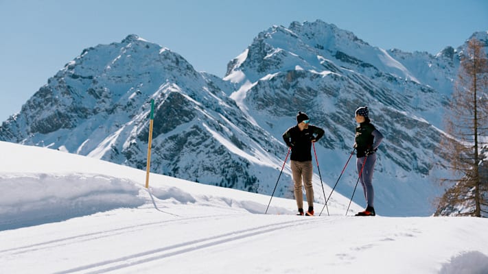 Das Paar fährt mit Langlaufski eine Loipe in der Schweiz bei Sonnenschein ab.