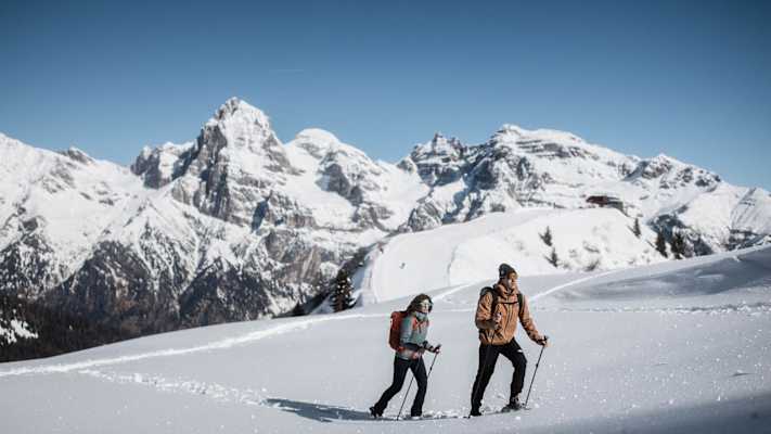 Frau und Mann beim Winter- und Schneeschuhwandern in Gossensass mit Bergen im Hintergrund.