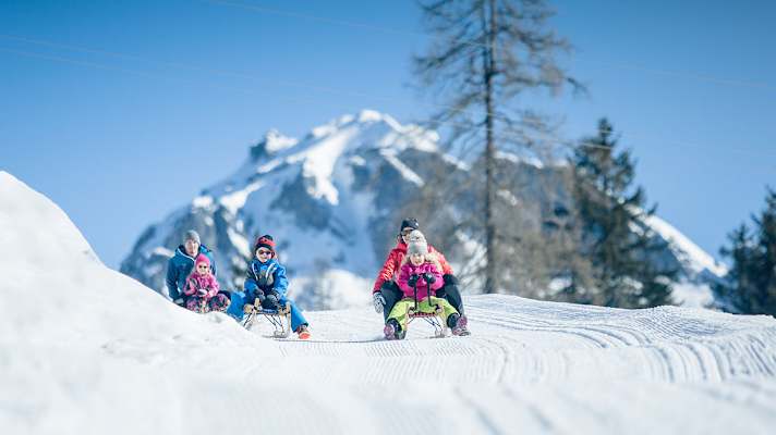 Eltern rodeln mit ihren Kindern eine präperierte Piste hinab.
