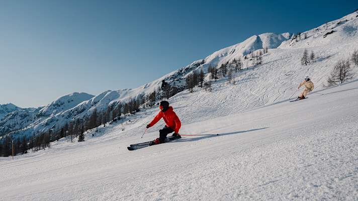 Zwei Skifahrer fahren eine perfekt präparierte Piste am Zauchensee hinunter.