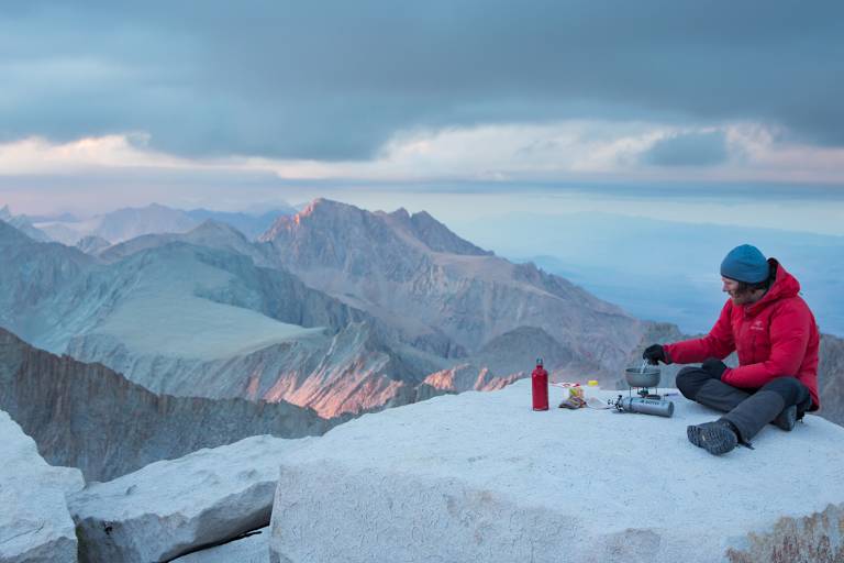 Mann kocht mit SOTO Kocher auf Berg Essen mit Panorama über Berge.