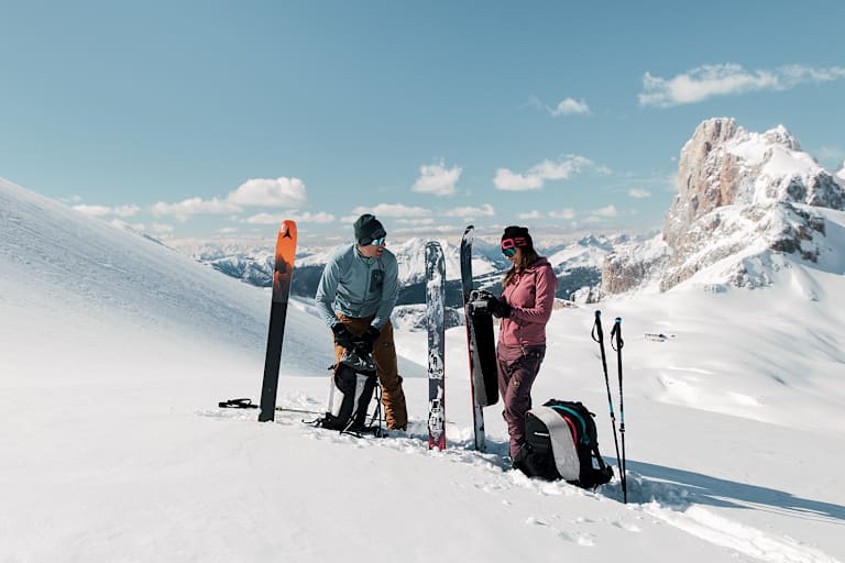Eine Frau und ein Mann stehen im Schnee auf einem Berg und machen sich für das Skifahren bereit.