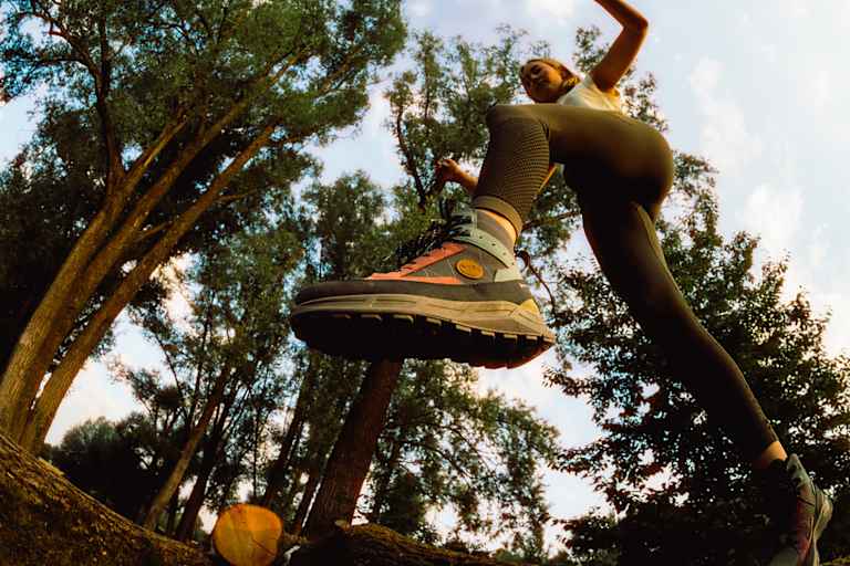 Frau springt im Wald über einen Baumstamm mit dem Hanwag Rotpunkt Light Mid GTX – leichter, vielseitiger Outdoor-Schuh für Alltag und Wanderungen