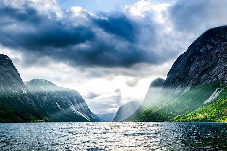 Norwegischer Fjord bei Sonnenaufgang mit schroffen Klippen und Wald 