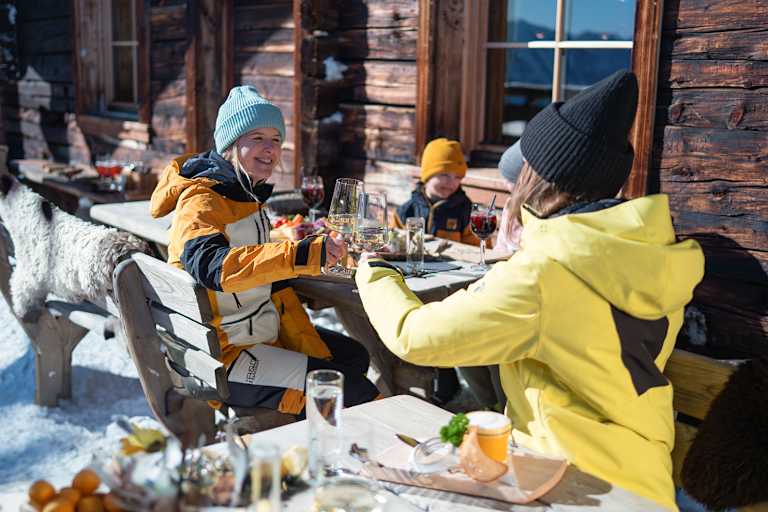 Zwei Damen stoßen mit einem Glas Wein auf der Skihütte im Winter an.