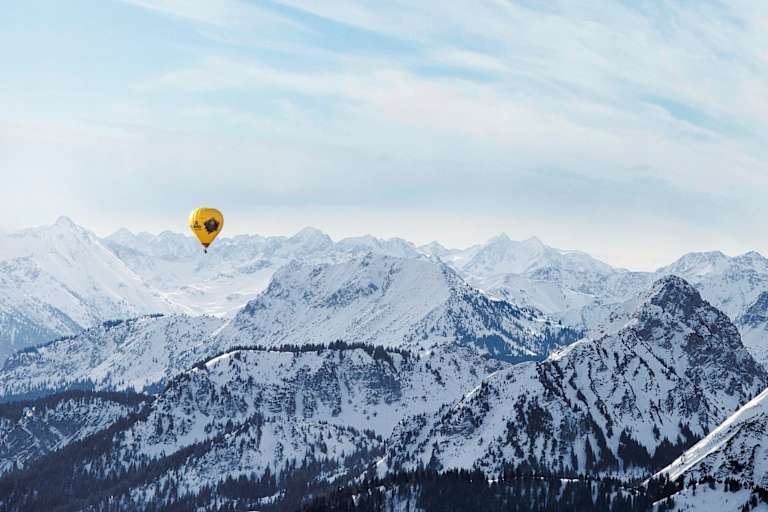 Ein gelber Heißluftballon, dahinter die schneebedeckten Alpen