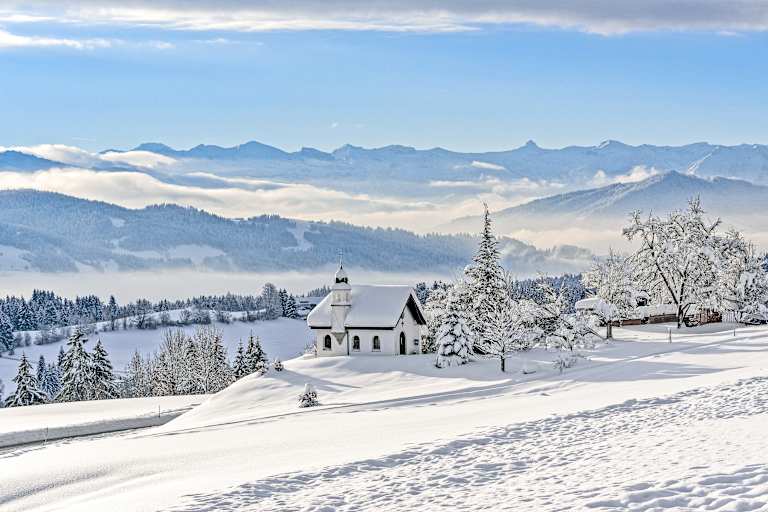 Die Hubertuskapelle in Scheidegg im Allgäu inmitten einer tief verschneiten Berglandschaft.