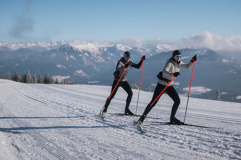 Zwei Langläufer auf einer Loipe in der neuen Nordic Kollektion von Löffler.