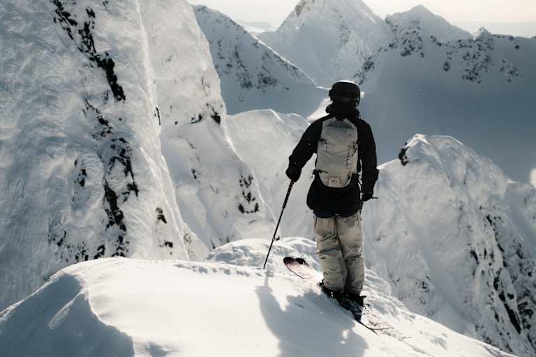 Ein Freerider steht auf einem Hang und blickt den verschneiten Berg hinab.