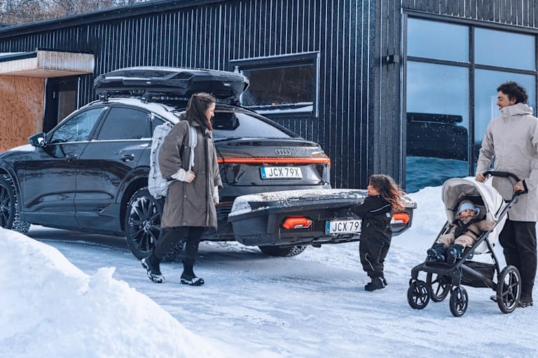 Eine vierköpfige Familie steht vor ihrem Auto, auf dem eine Thule-Heckbox befestigt ist.