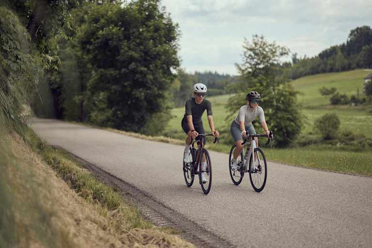 Zwei Radfahrer fahren auf einer ruhigen Landstraße im Mühlviertel bei der Bike Experience, umgeben von grüner Natur und sanften Hügeln.