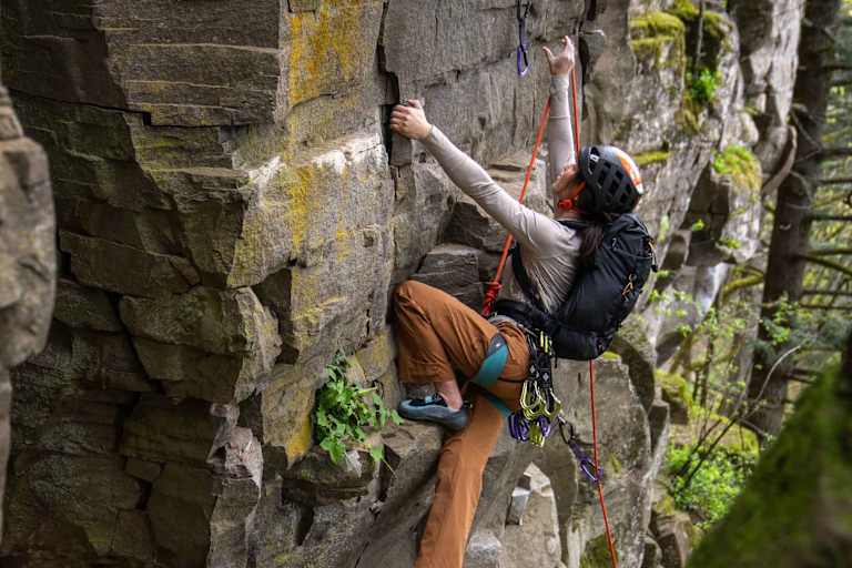 Eine Frau klettert auf einen Felsen mit dem neuen Gregory Rucksack Alpinisto 30.