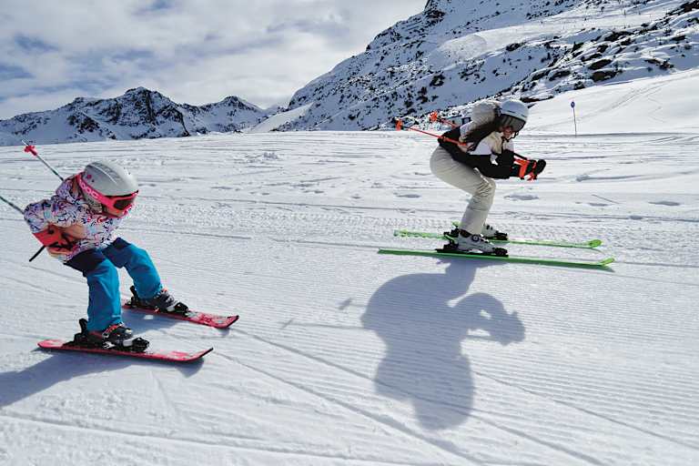 Eine Frau und ein Mädchen fahren gemeinsam Ski und nehmen dabei die Schussposition ein.