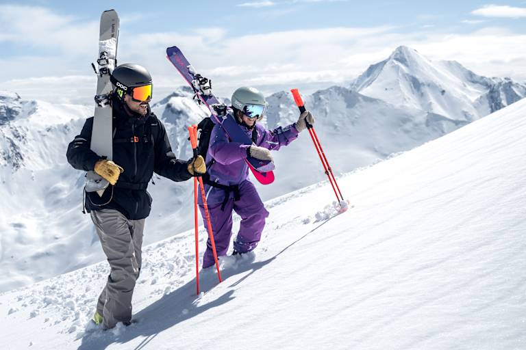 Ein Skifahrer und eine Skifahrerin gehen eine Piste in Ischgl hinauf.