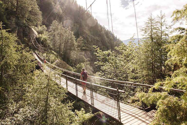 Eine Frau geht eine Hängebrücke in der Region Naturns entlang.