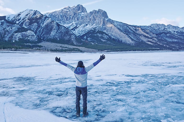 Ein Mann steht vor einem Berg im Schnee mit offenen Armen.