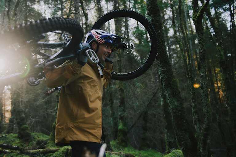 mann hat sein mountainbike auf den schultern, im wald