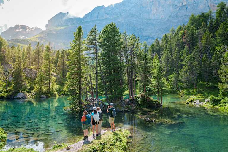 Vier Wanderer am Arvenseelo in der Schweiz, umgeben von Wasser und Wäldern.