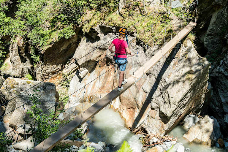 Mädchen im Klettersteigset beim Balancieren auf einem Baumstamm in der Feeschlucht
