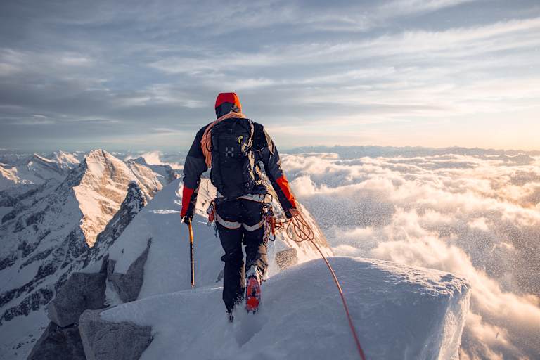 mann beim bergsteigen auf bergspitze, gekleidet in haglöfs