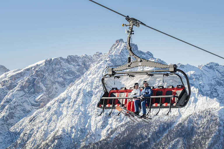 Ein Skilift in den verschneiten Bergen mit 2 Personen, die drinnen sitzen.