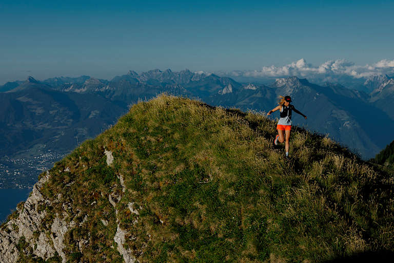 Eine Frau läuft auf einem Berg in einer alpinen, sommerlichen Kulisse.