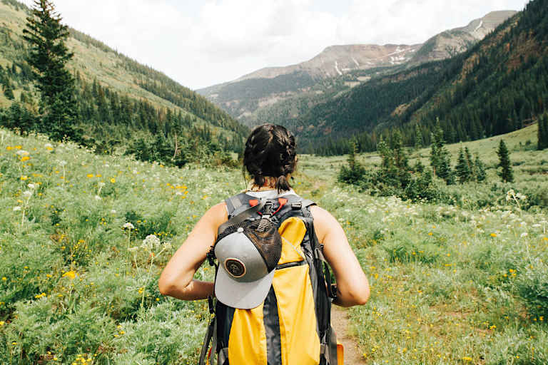 Eine Frau mit einem gelben Wanderrucksack spaziert durch eine bergige Landschaft.