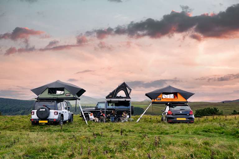 Zu sehen sind drei Autos auf einer Wiese auf denen drei unterschiedliche Tentbox Dachzelte montiert sind.