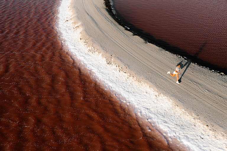 Eine Frau läuft einen sandigen Weg entlang inmitten eines braun-rötlichen Gewässers.